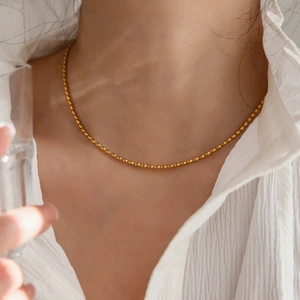 Nahaufnahme einer goldenen Kugelkette am Hals getragen mit weißer Rüschenbluse