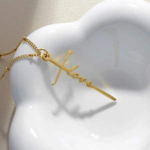 Collier en acier titane doré avec pendentif Love et croix sur un plateau blanc