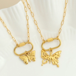 Detail of gold butterfly necklaces with paperclip chains on a wavy ceramic base