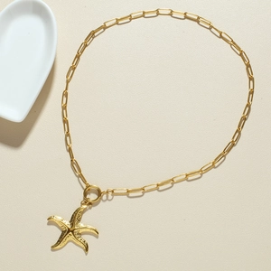 Gouden paperclip ketting met getextureerde zeester hanger op een beige achtergrond