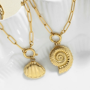 Gouden paperclip ketting met schelp en nautilus hangers op een keramisch bordje