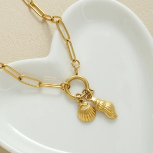 Detailopname van gouden paperclip ketting met schelphangers op een hartvormig dienblad