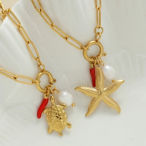 Collana dorata con ciondoli tartaruga marina stella marina e perle in un piatto a conchiglia