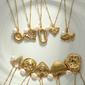 Detailed macro view of assorted gold heart and leaf pendants with pearls on white tray