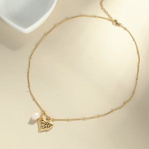 Golden bead necklace with hammered heart pendant and white pearl on beige surface
