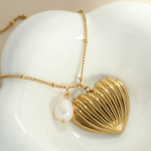 Macro shot of gold heart pendant with vertical texture and baroque pearl on gold chain