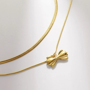 Detail of double-layer gold necklace showing herringbone chain and bow pendant