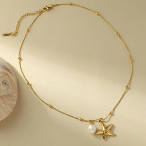 Dettaglio della collana con ciondolo a stella marina dorata e perla bianca su fondo