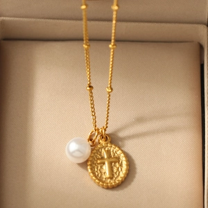 Détail du collier doré avec pendentif disque à croix en relief et perle blanche