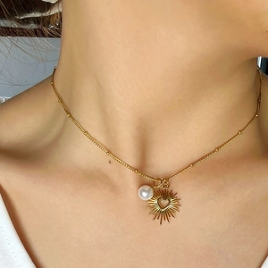Collier en acier doré avec pendentif cœur soleil et perle porté par un mannequin