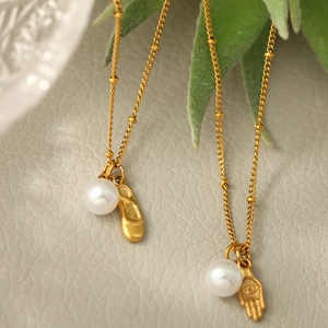 Détail macro de colliers dorés avec pendentifs perle et main de Hamsa sur cuir