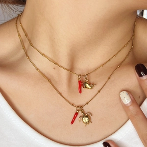 Primo piano di collana dorata a due strati con ciondoli a forma di peperoncino, balena e tartaruga
