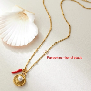 Collana con perle di conchiglia dorata con ciondolo rosso su sfondo bianco e conchiglia