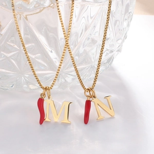 Close-up of gold box chain necklace with red chili pepper and letter M and N pendants