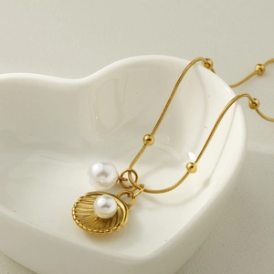 Macro detail of a gold seashell pendant with white pearls on a sleek snake chain