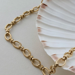 Vue macro d'un collier chaîne O plaqué or 18 carats avec maillons texturés sur un coquillage