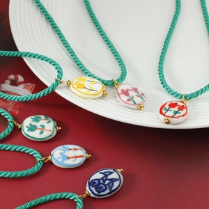 Handgemaakte keramische bloemenketting met groen gevlochten koord op een bordje