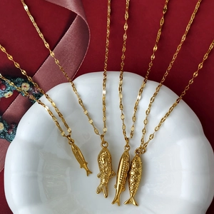 Detalle de cuatro colgantes de peces dorados en cadenas finas sobre un plato de cerámica