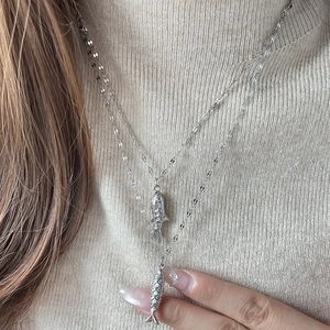 Collar de doble capa de plata con colgantes de peces sobre fondo de suéter de punto