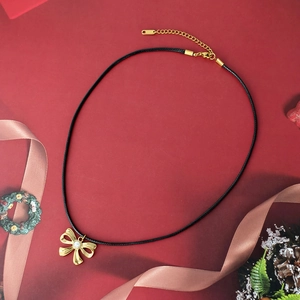 Collar con colgante de lazo dorado y perla con cordón negro sobre fondo rojo festivo