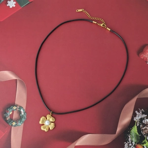 Detalle de colgante de flor dorada con perla en cordón negro sobre un fondo festivo