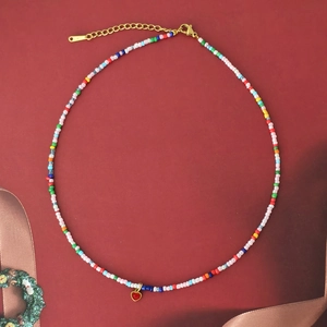 Bunte Boho-Perlenkette mit rotem Herzanhänger auf dunkelrotem Hintergrund präsentiert