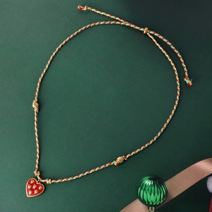 Handwoven cord necklace with red heart pendant and gold accents on festive background