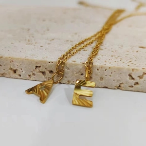 Detailed macro view of gold-plated letter pendants A and E with sunburst engraving texture