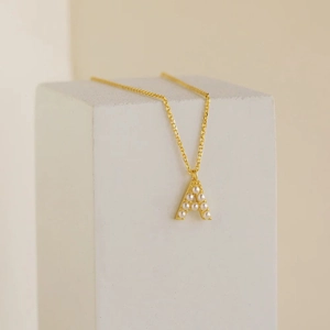 Detail of gold letter A pendant with inlaid pearls on a minimalist chain necklace