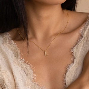 Elegant gold necklace with pearl-inlaid letter L pendant worn on a model's neck