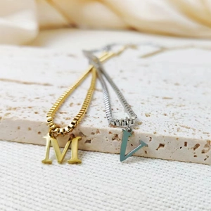 Macro shot of gold M and silver V letter pendants on stainless steel box chains