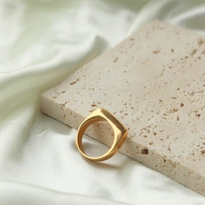 Detailed close-up of a minimalist 18K gold-plated signet ring on stone and silk background