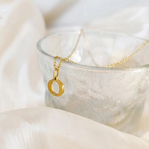 Macro shot of gold letter O pendant necklace on soft white silk with glass detail