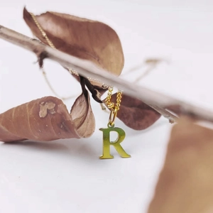 Close-up of golden letter R pendant on a bead chain hanging on natural branches