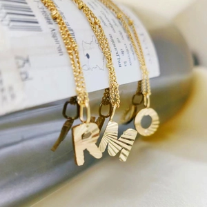 Gouden titanium stalen ketting met letterhangers R M O en gestructureerde afwerking
