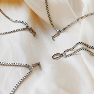 Detailed view of silver box chain necklaces featuring dimensional E, L, O, V initial pendants