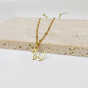 Detailed view of a gold-plated cursive letter W pendant on a delicate beaded satellite chain