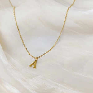 Detail of a gold letter A pendant necklace on a minimalist soft white silk fabric
