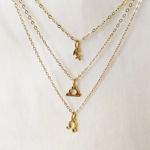 Detailed view of triple-layered gold necklaces with Sagittarius Libra and Leo zodiac pendants