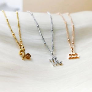 Trois colliers 12 signes du zodiaque en finitions or, argent et or rose sur tissu beige