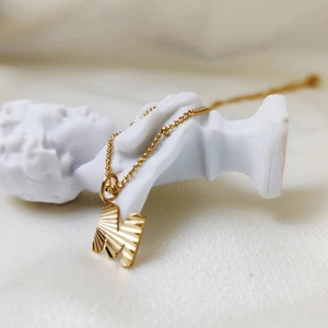 Detailweergave van gouden ketting met een getextureerde M-hanger aan een kralenketting