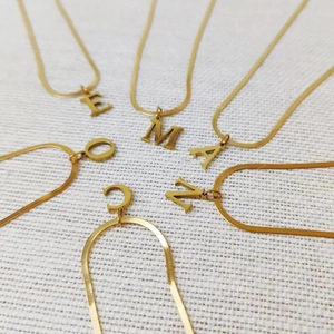 Flat snake bone chain necklaces with 18K gold-plated initial letter pendants on white fabric