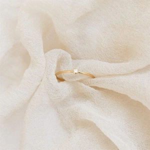 Macro detail of minimalist gold ring with crystal inlay on soft textured fabric background