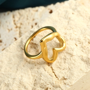 Makro-Detail eines goldenen Edelstahl-Herzrings auf einem strukturierten Natursteinboden