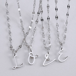 Gepolijste zilveren LOVE letter hanger ketting set met holle hart details op platte achtergrond