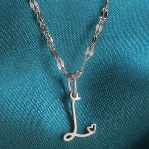 Macro-opname van de zilveren letter L hart hanger aan een gedraaide glanzende ketting