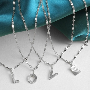 Detailed close-up of silver initial pendants with textured radial pattern on fine chain