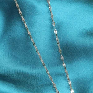 Polished silver thin link initial necklace chain on blue silk background macro view