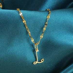 Detail van gouden ketting met letter L-hanger en hartje op donkerblauwe zijde