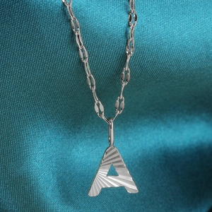 Macro view of silver letter A pendant with sunray texture on blue silk background